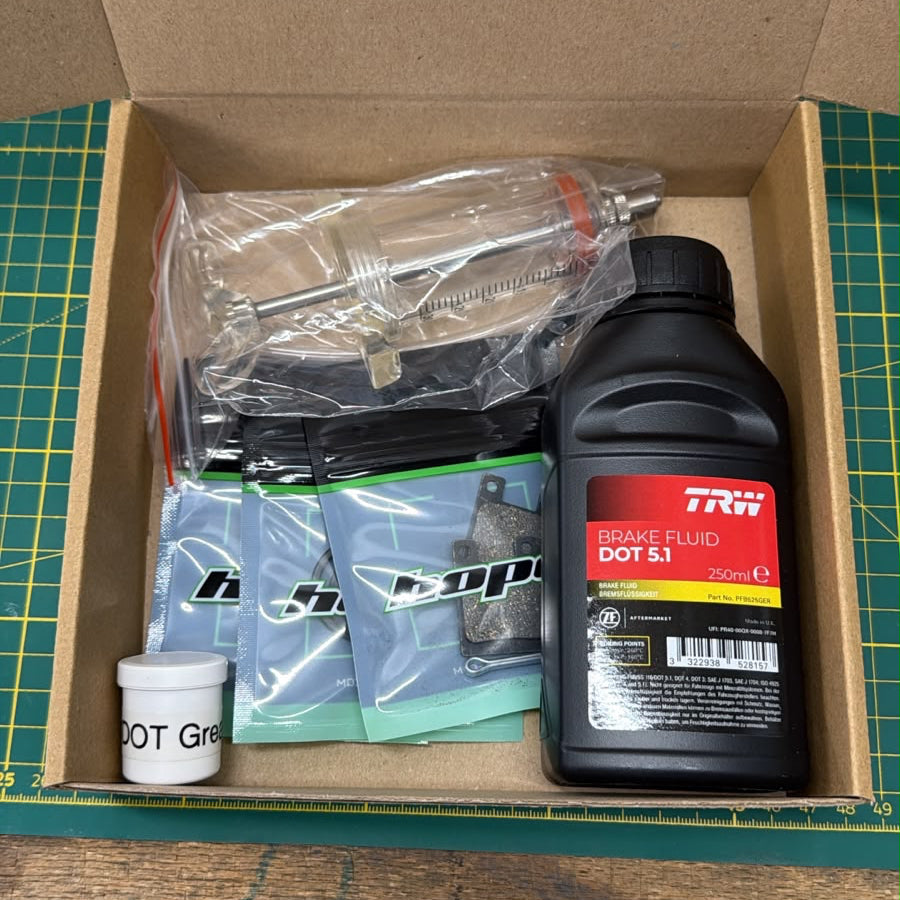Ollis Hope C2 brake service kit in cardboard box with DOT 5.1 brake fluid, DOT grease, bleeding syringe and hose, brake pads and seal kits for Porsche FS Evolution.